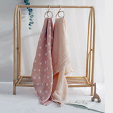 Salmon Poppy muslin swaddle and cream blanket hanging on a wooden rack